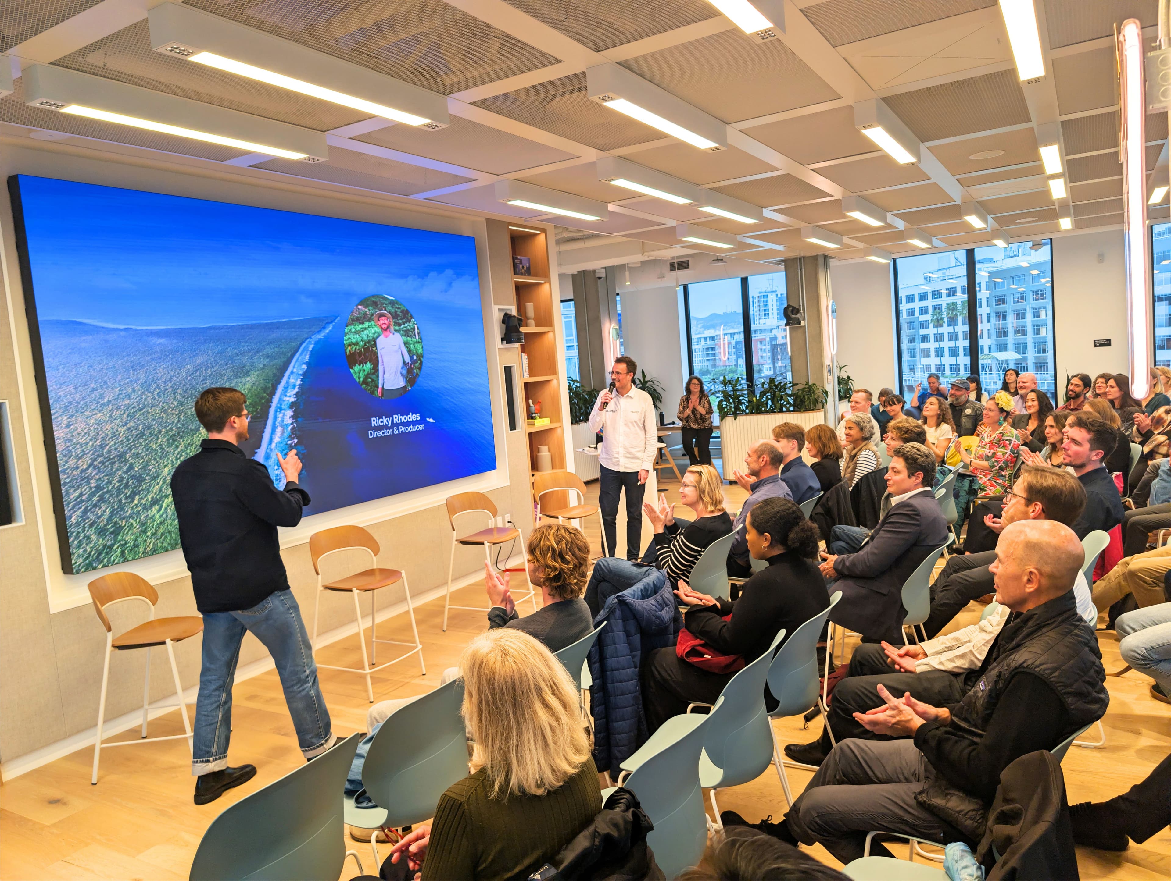 Ricky Rhodes speaking at SF Climate Week 2026 with audience applauding, Impossible Cleanups slide visible behind